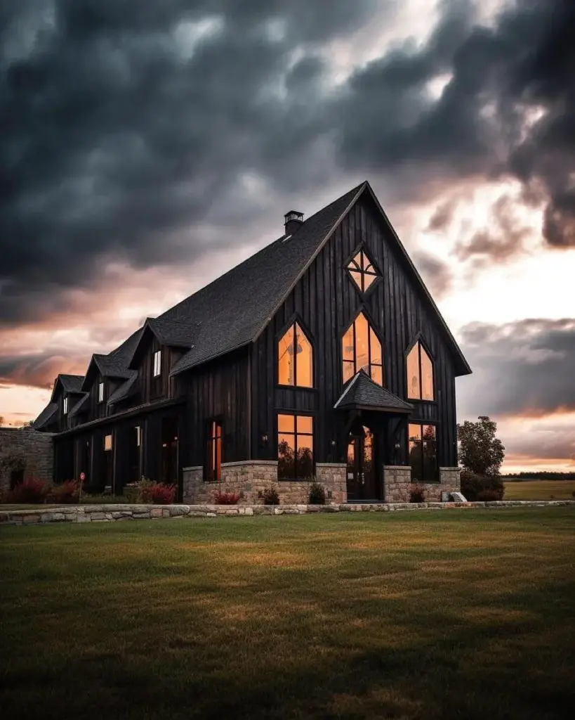 Black modern barn house glowing against stormy sunset sky