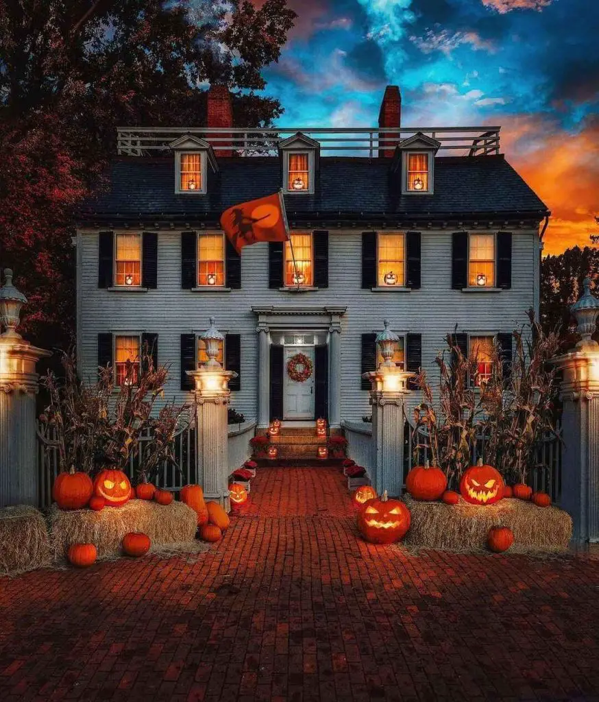 Colonial house decorated with pumpkins and Halloween lights at sunset