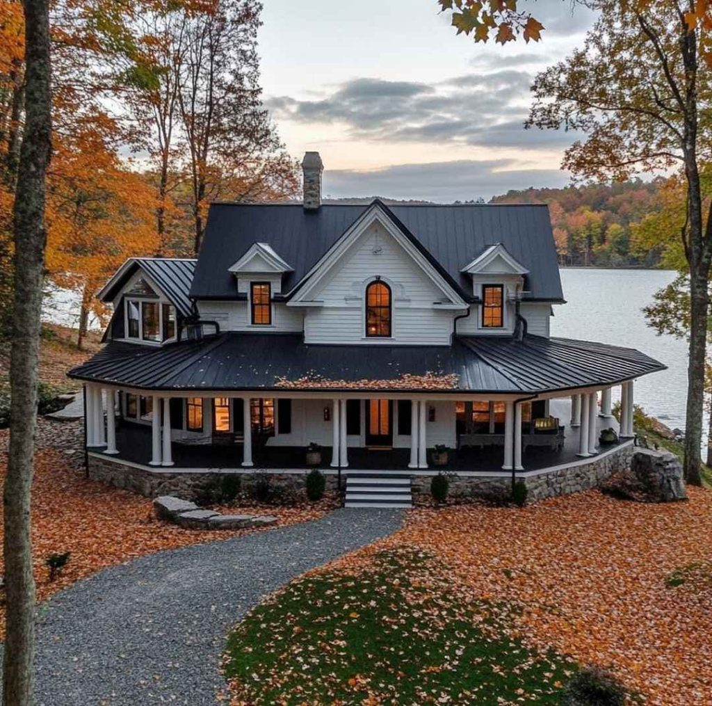 Modern farmhouse with black metal roof wraparound porch overlooking lake in fall foliage