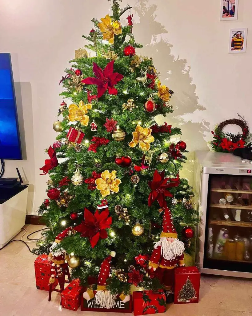 Christmas tree decorated with golden magnolias red poinsettias and festive gnomes surrounding wrapped presents