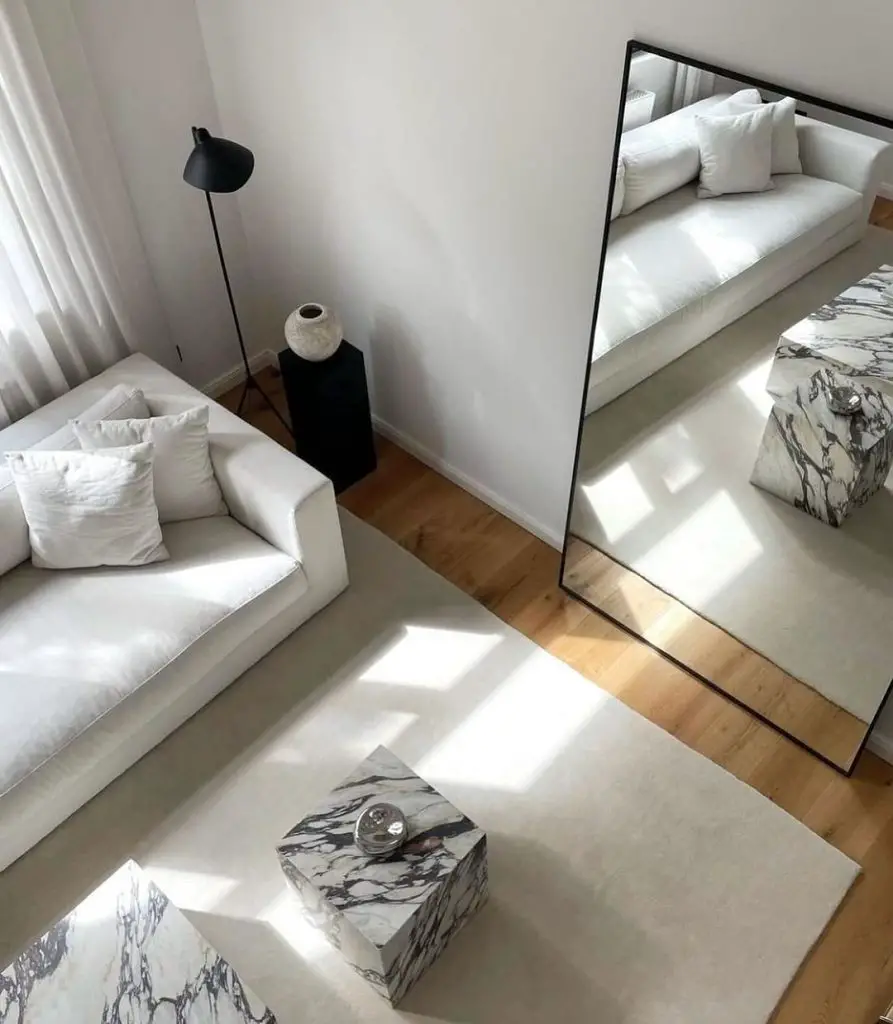 Minimalist white living room with a large mirror, white sofa, black floor lamp, and marble cube side