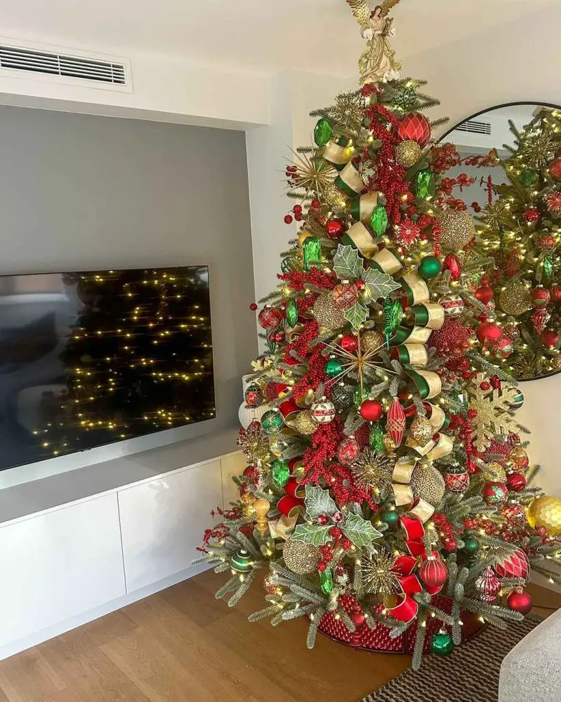 Christmas tree decorated with angel topper red green and gold ornaments beside modern TV unit