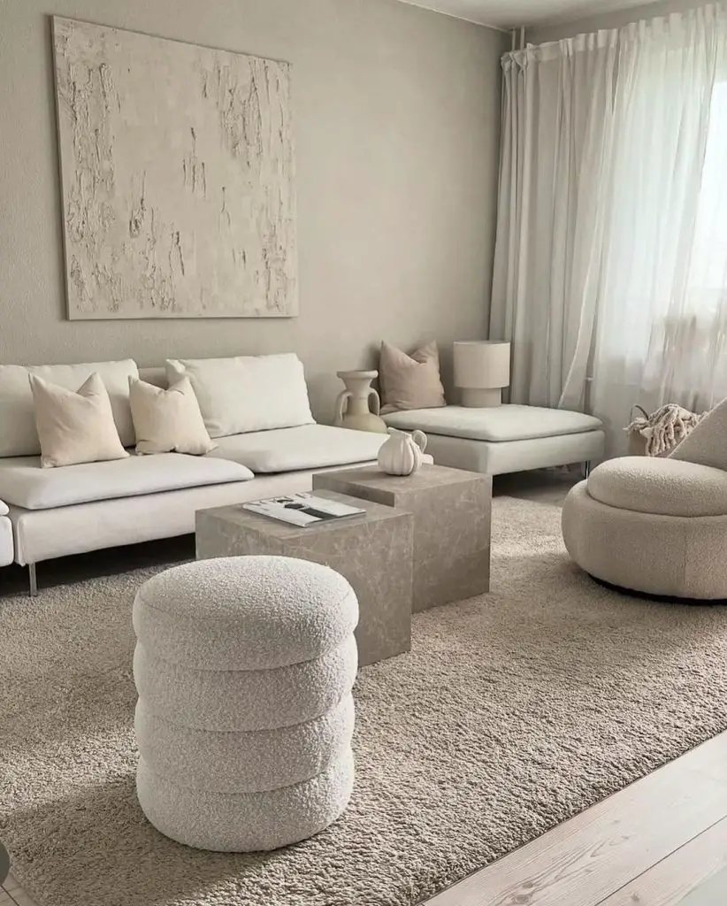 A minimalist living room in cream and beige tones, featuring a textured wall art, sleek sofa, stone coffee tables