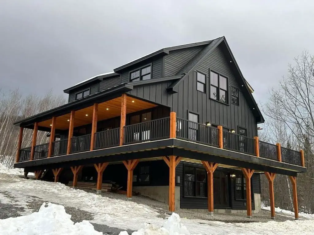 Black barn house with wraparound deck in snowy mountains
