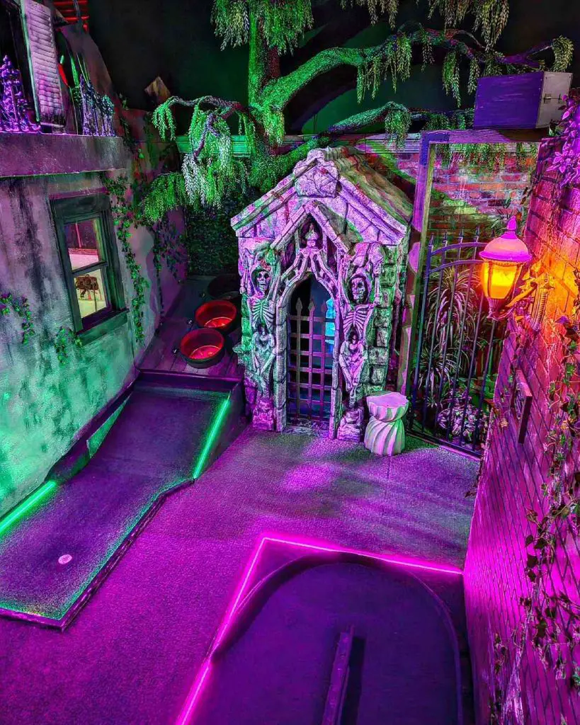 Colorfully lit Halloween-themed mini-golf course with spooky decorations.