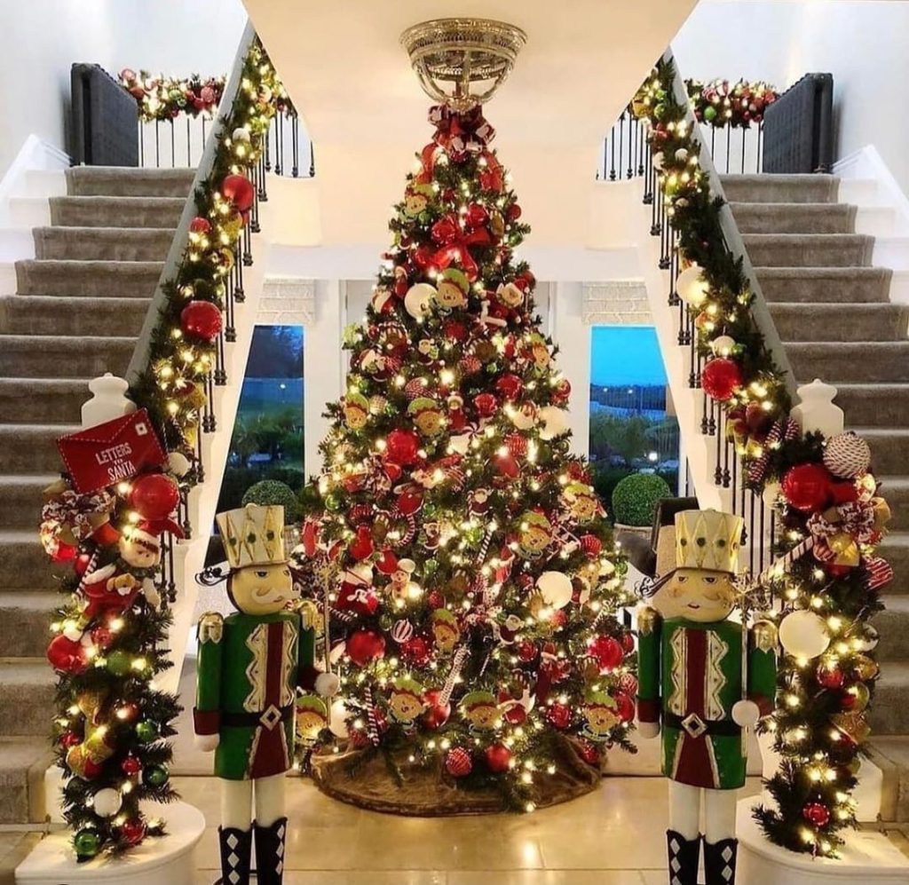 Grand Christmas tree flanked by life-size nutcrackers and decorated staircases in luxurious white foyer