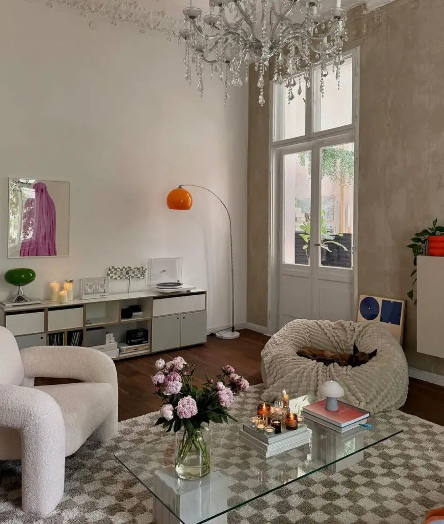 Eclectic living room with crystal chandelier, white curved chair, oversized bean bag, glass coffee table