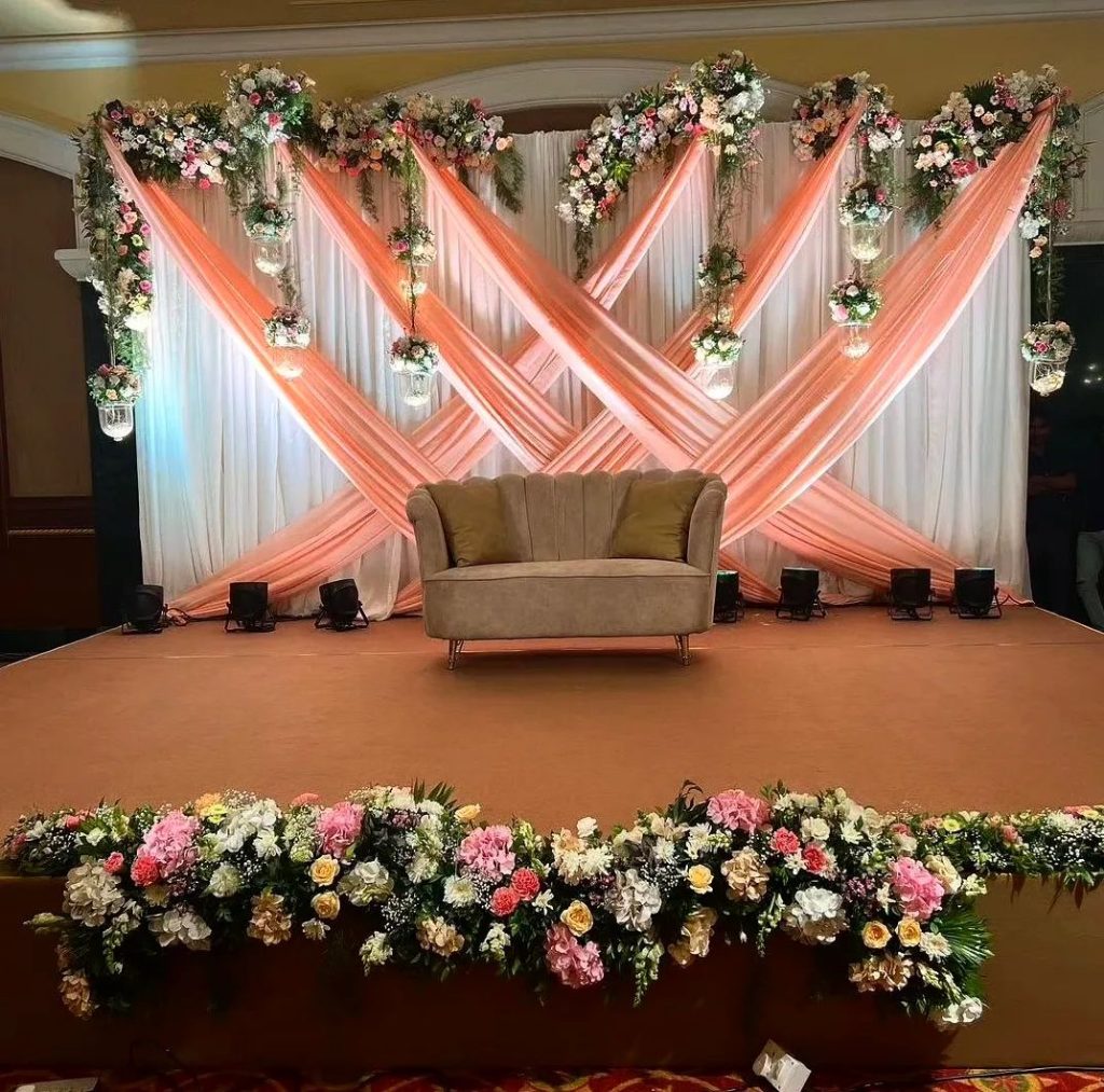 Peach draped wedding backdrop with floral accents and velvet loveseat