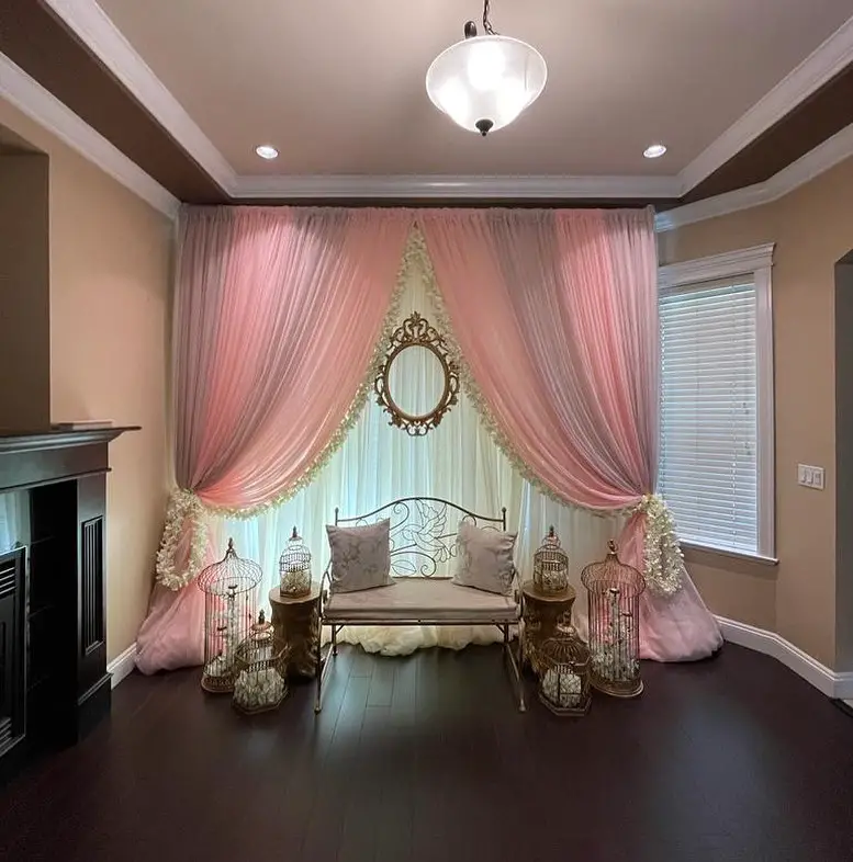 Pink draped alcove with carved wood bench under chandelier light.
