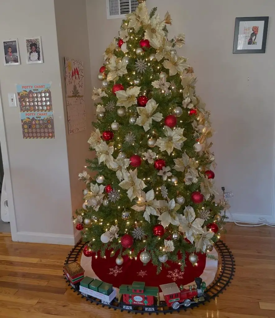 Christmas tree decorated with cream poinsettias and red ornaments surrounded by classic toy train set