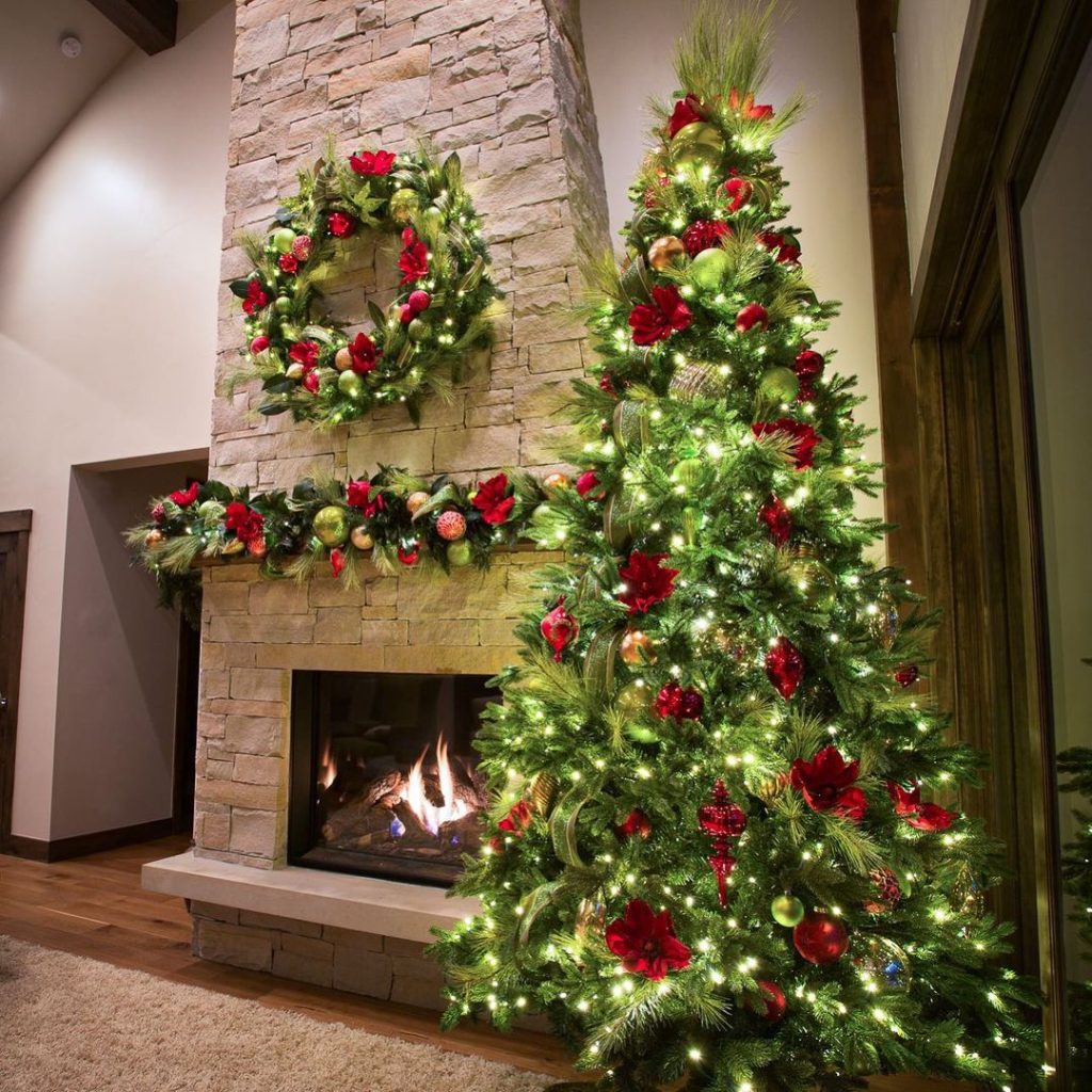 Christmas tree with red poinsettias and green ornaments beside stone fireplace