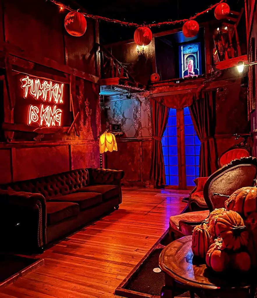 Red-lit Halloween-themed lounge with vintage furniture and pumpkin decorations.