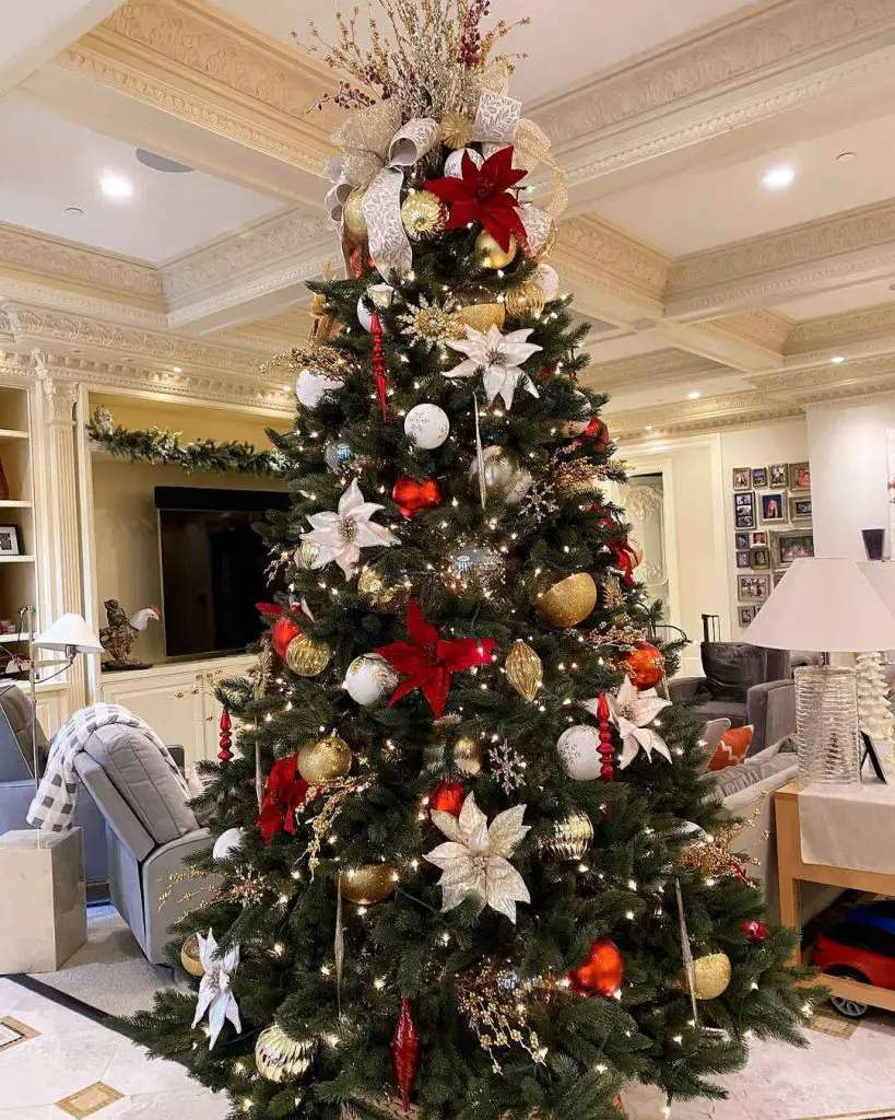 Majestic Christmas tree decorated with red white and gold ornaments beneath detailed crown molding