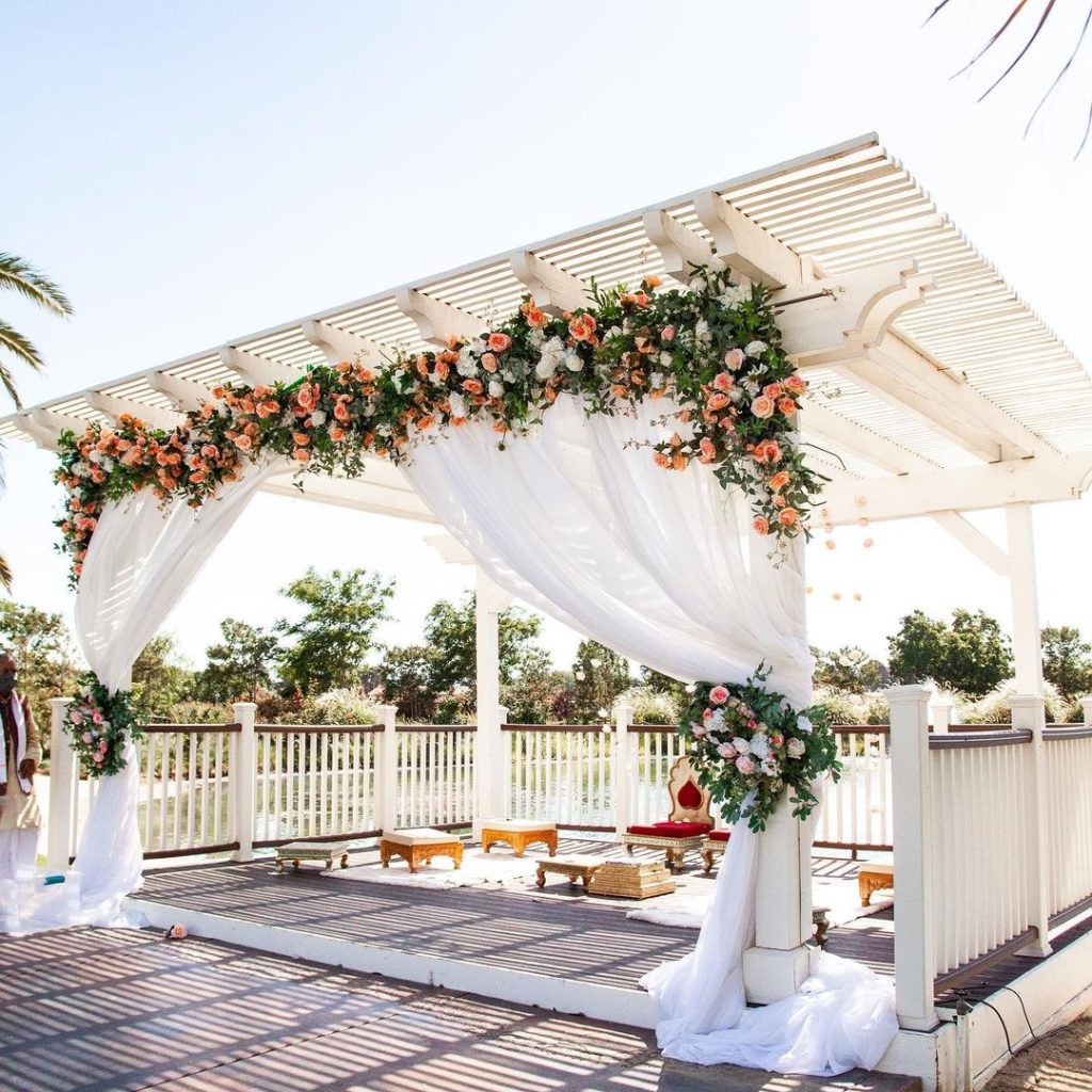 Wedding ceremony under floral draped wooden pergola with seating.