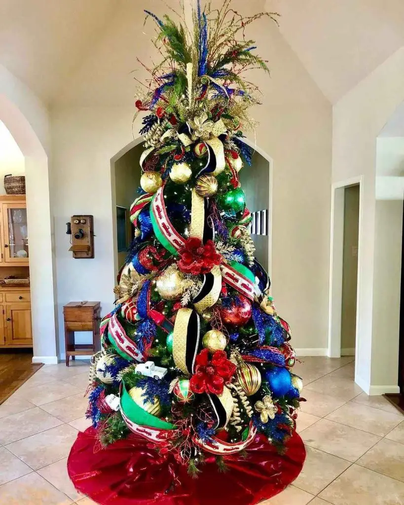 Elegant Christmas tree with royal blue, gold ribbons, vintage ornaments, and red poinsettias against white archway