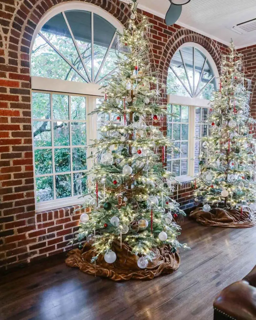 Christmas trees by arched windows in brick-walled room