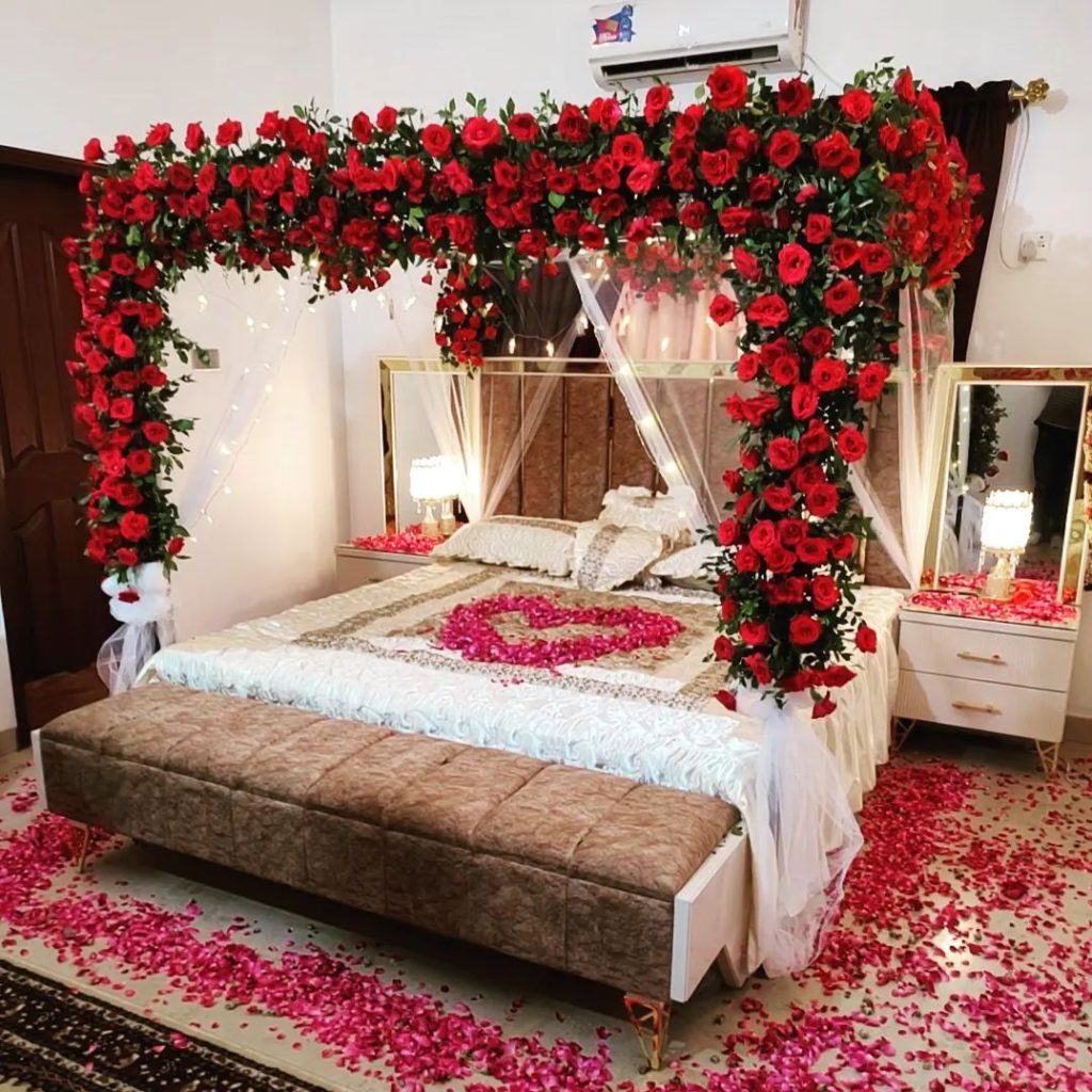 A bed covered in rose petals with floral decor around a romantic bedroom scene.