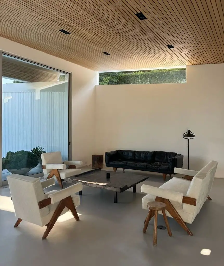 A minimalist living room with mid-century modern furniture, featuring cream armchairs, a black leather sofa