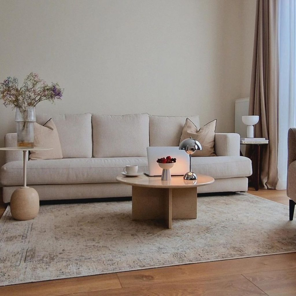 Minimalist living room with cream sofa, round wooden coffee table, and neutral decor.