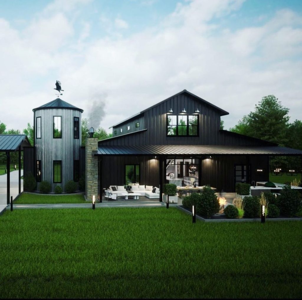 Modern black barn house with cylindrical silo tower featuring outdoor living space and landscape lighting