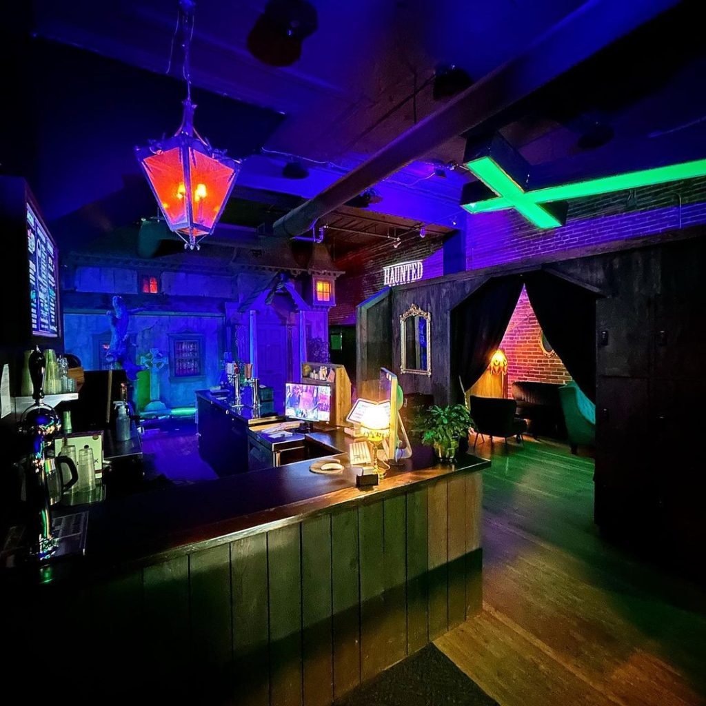 Dimly lit Halloween-themed bar with spooky decorations and neon lights.