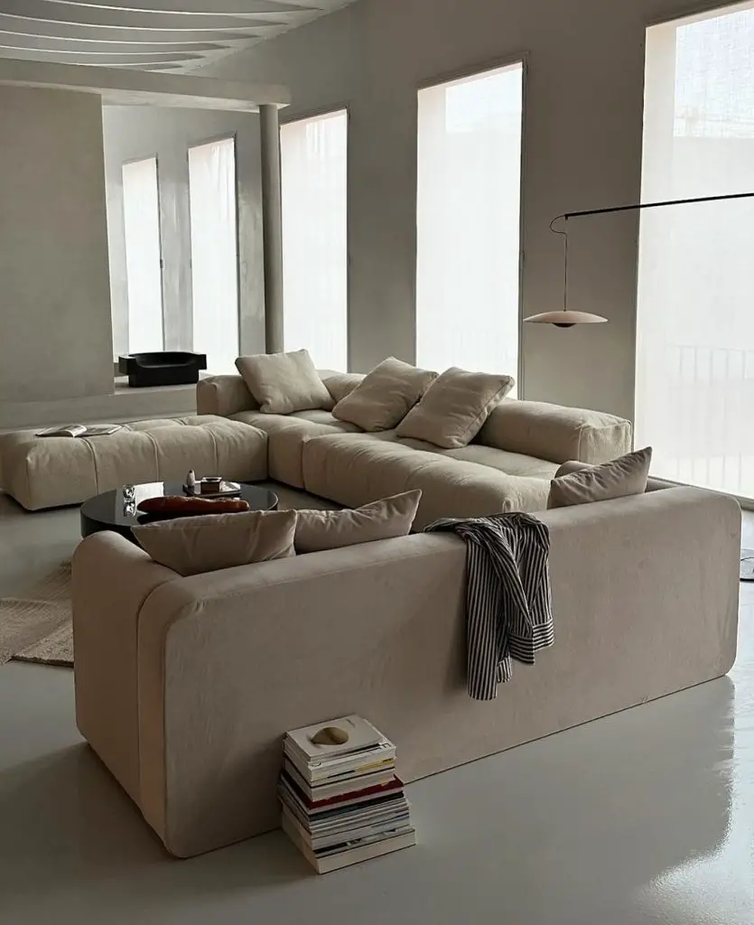 Minimalist living room with large beige sectional sofa, black round coffee table