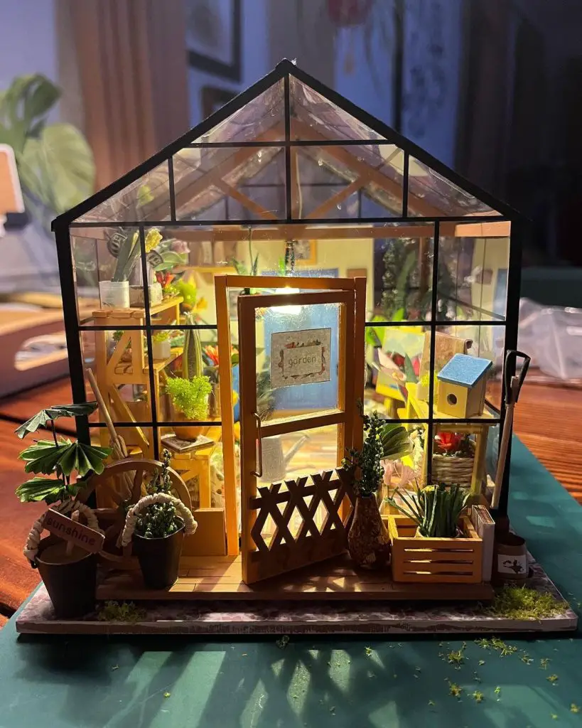 Illuminated miniature greenhouse diorama with tiny plants and gardening accessories