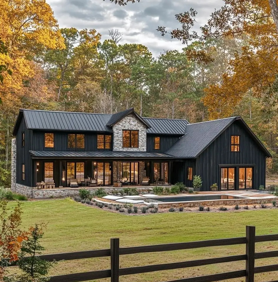 Modern black farmhouse with stone accents pool and split-rail fence in autumn forest setting