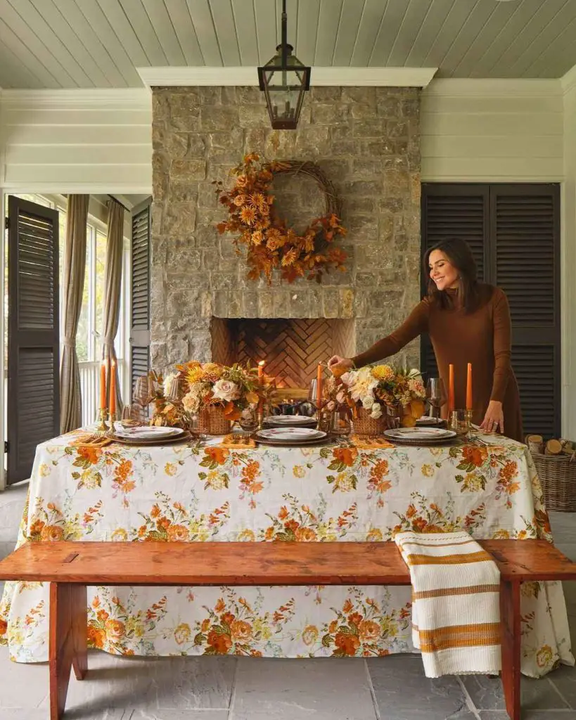 Autumn porch dining setup with stone fireplace fall wreath and orange floral tablecloth