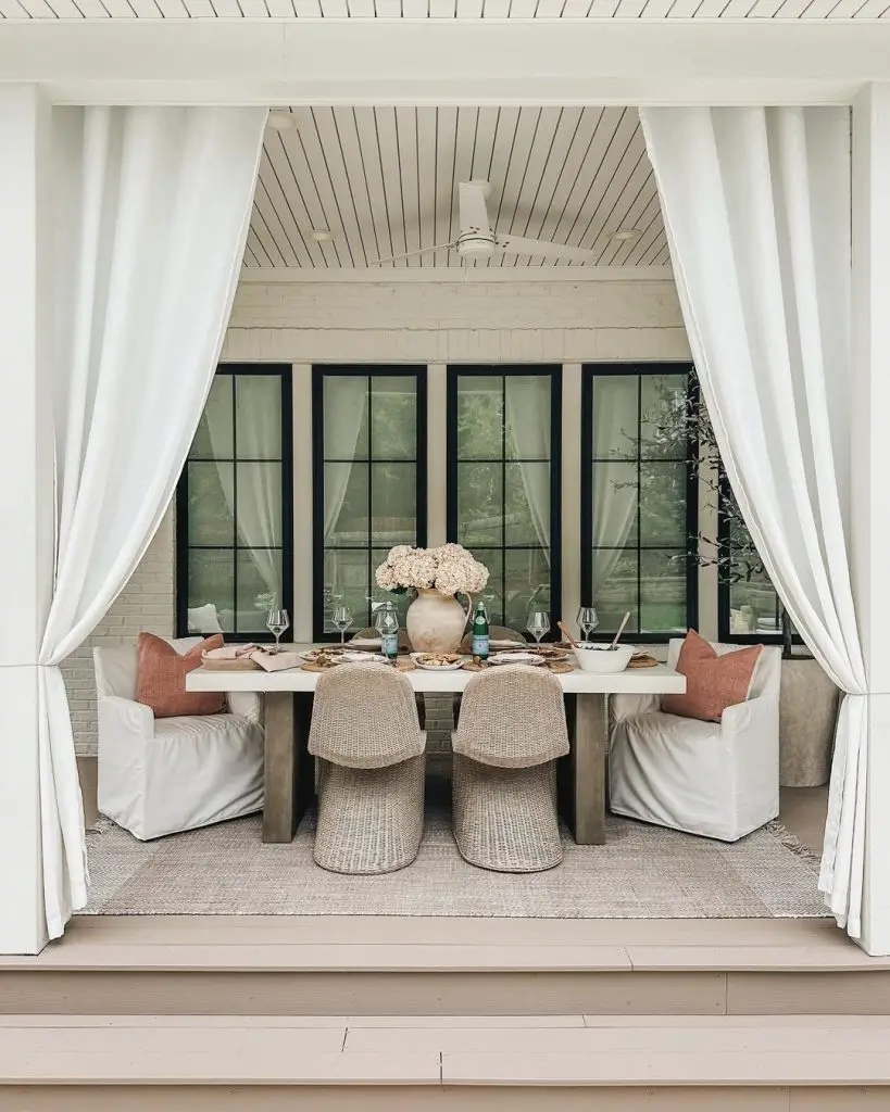 Sunlit dining nook with white curtains rattan chairs and modern concrete table against black windows