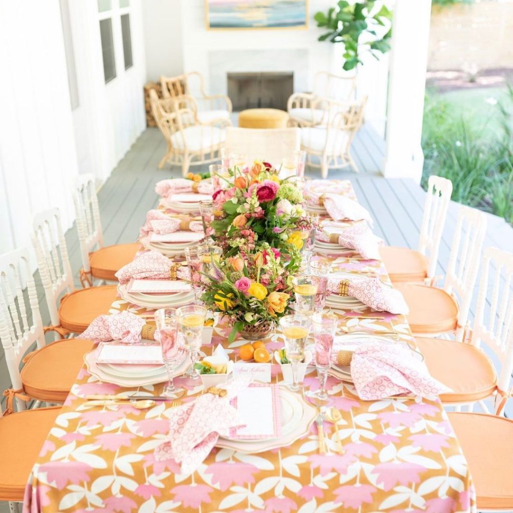 Bright pink and orange tablescape with citrus accents and mixed florals on breezy porch