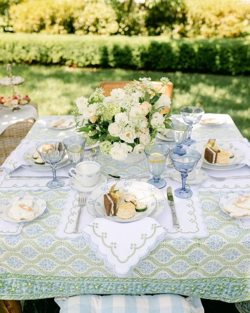 Garden tea party with vintage blue glassware, white floral centerpiece, and French-inspired table linens