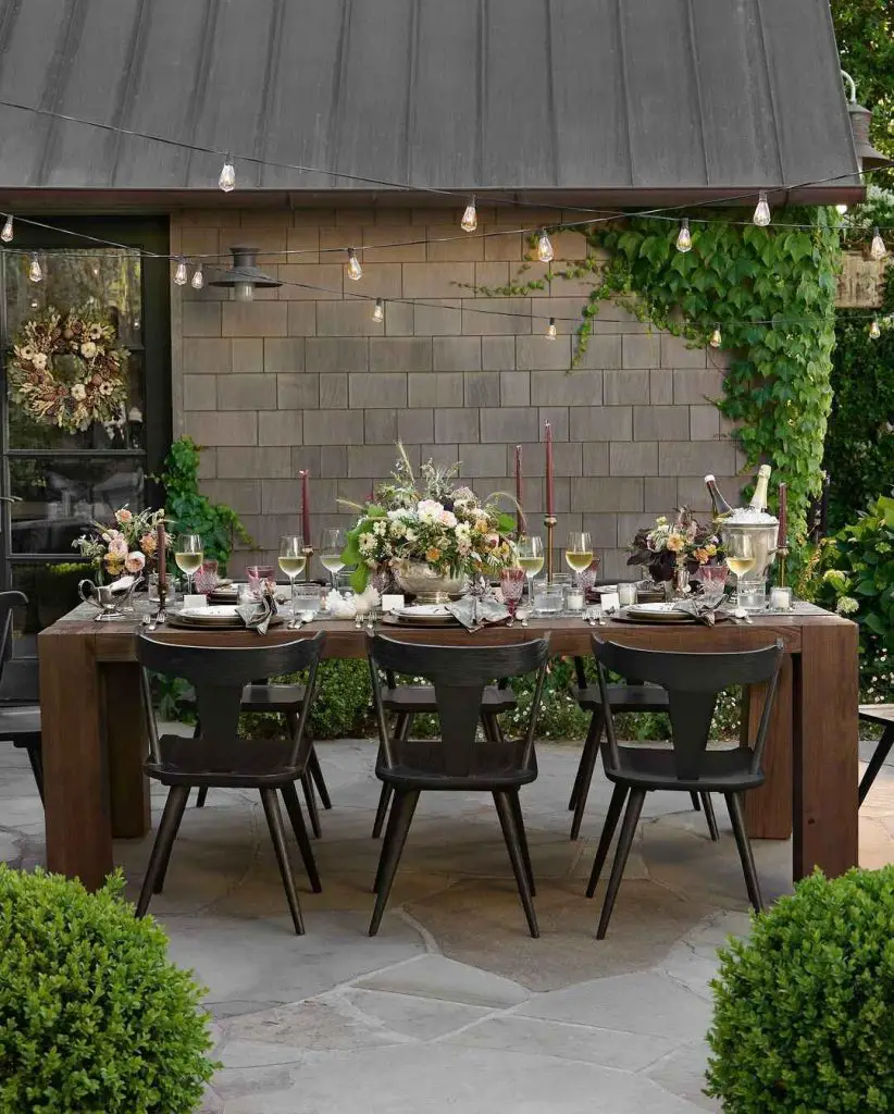 Outdoor dining setup with string lights and garden backdrop