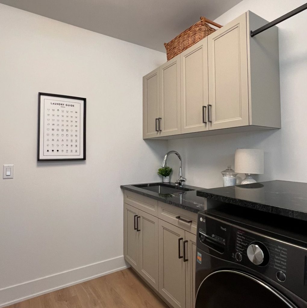 Compact beige laundry room with black counters and care guide display