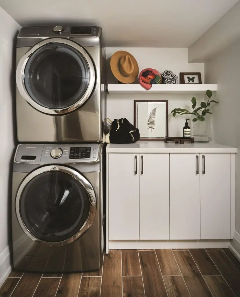 Compact laundry space with stacked silver appliances wooden floors and minimal white storage