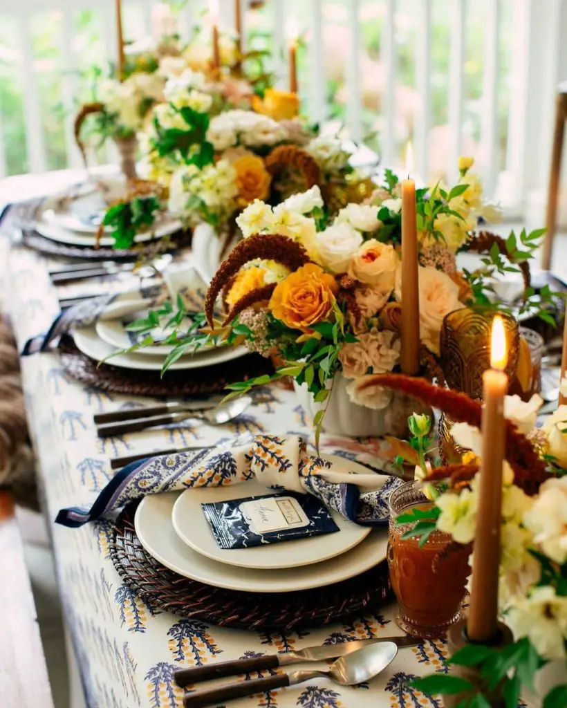 Elegant table setting with blue-patterned linens, amber candles, and golden roses
