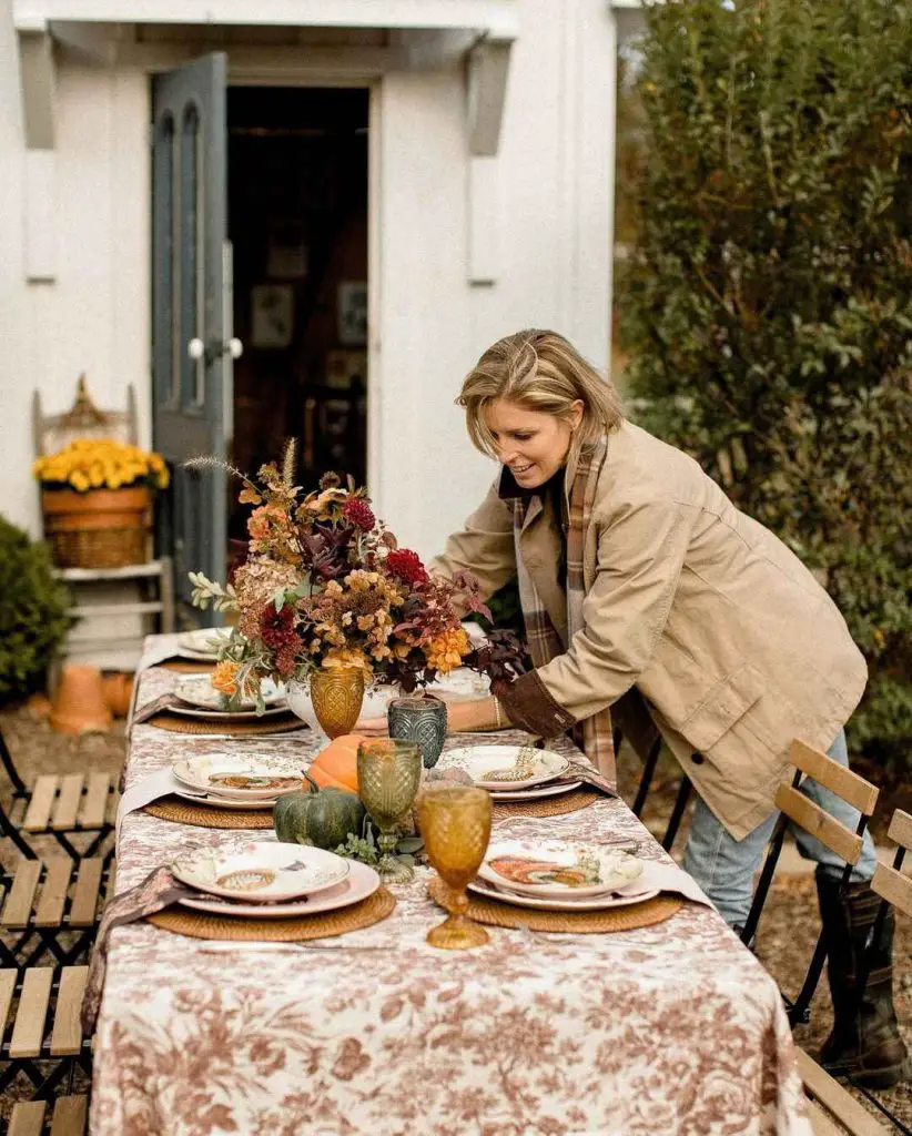Woman arranging elegant outdoor fall table with vintage decor and autumn florals