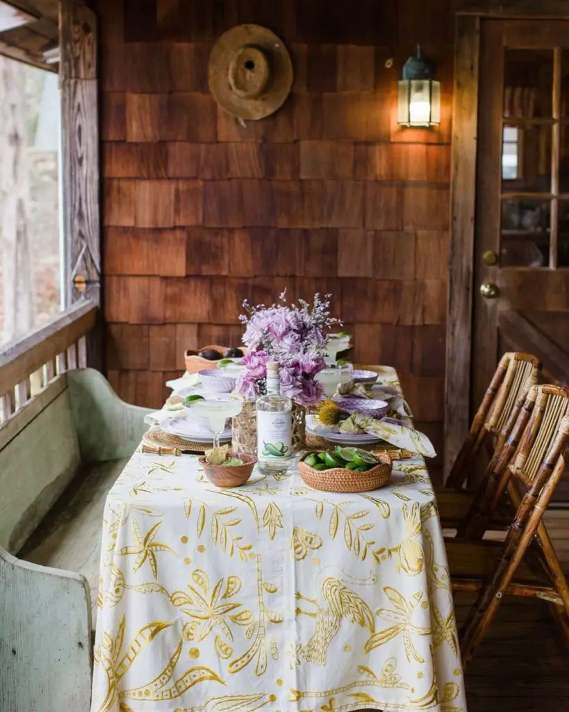 Cozy cabin porch dining setup with tropical tablecloth purple flowers and margarita essentials