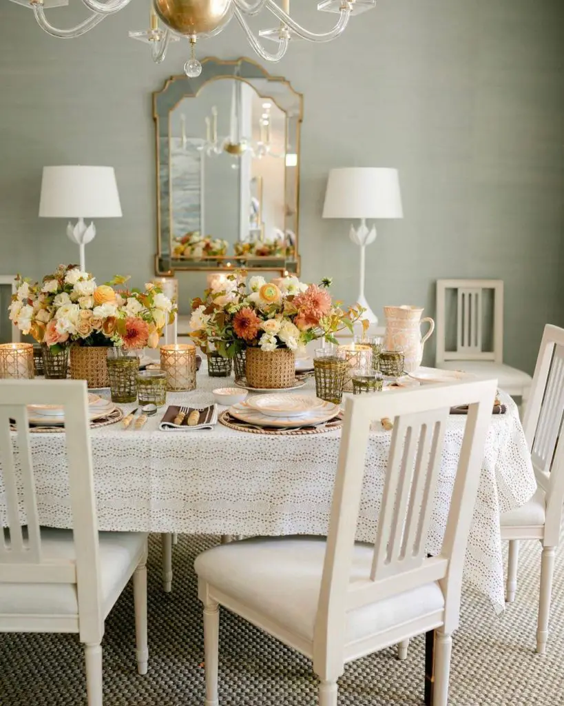 Elegant dining room with peach floral arrangements brass accents and eyelet tablecloth against sage green walls