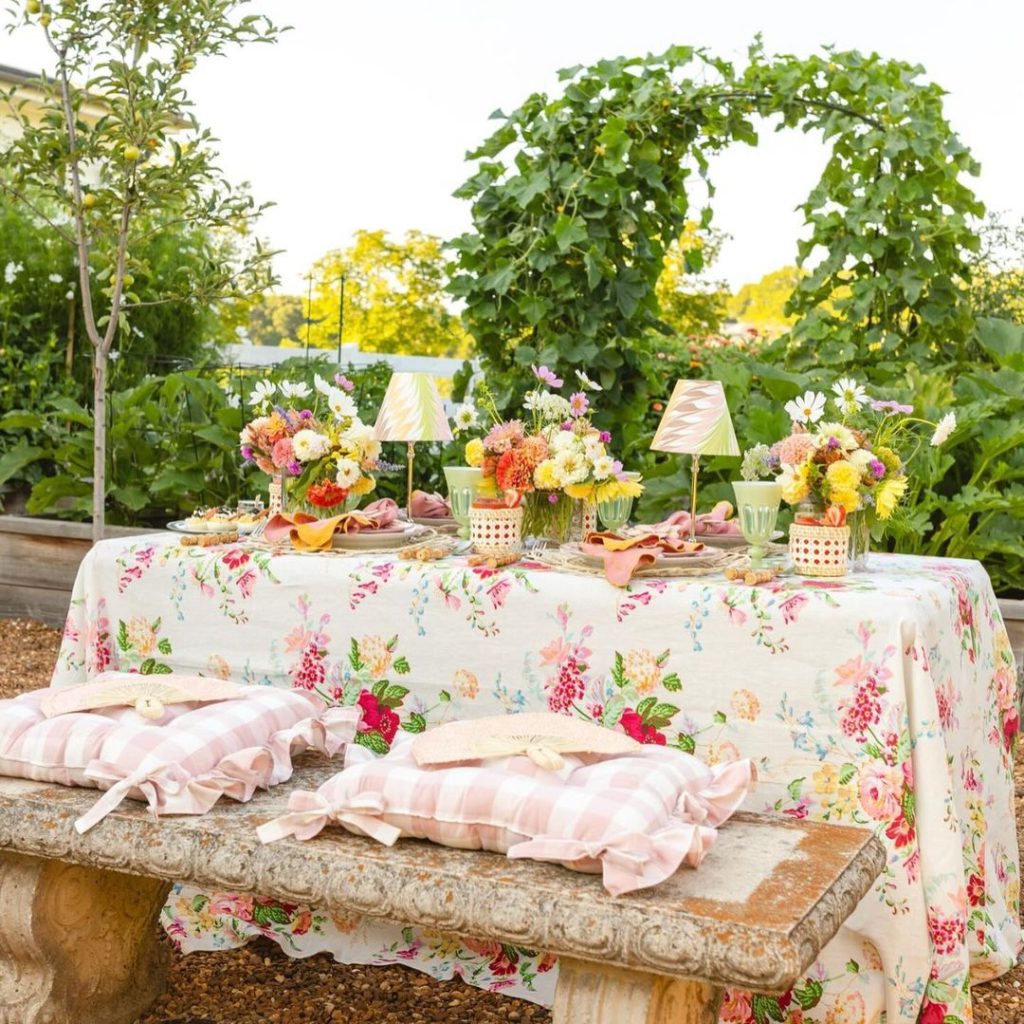 Romantic garden tablescape on stone bench with floral linens and pink cushions