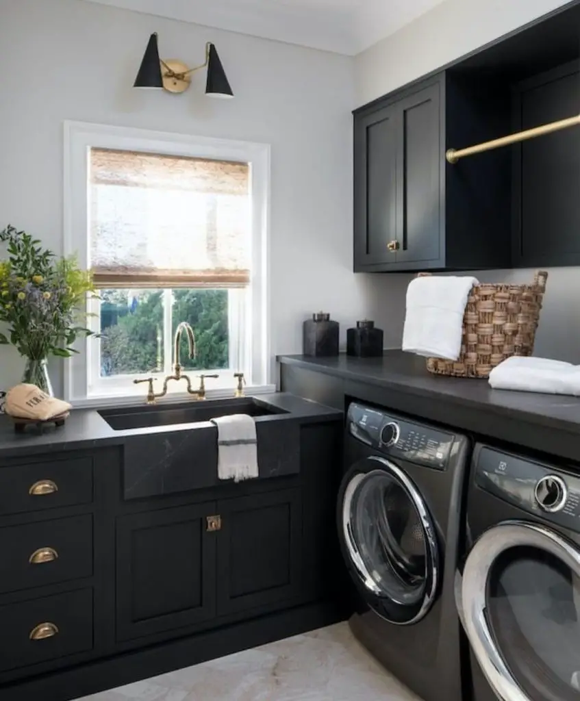 Modern black laundry room with farmhouse sink, brass fixtures, and built-in storage solutions