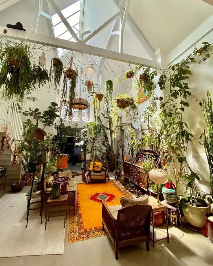 Bright vaulted-ceiling room filled with hanging plants crystal chandeliers vintage furniture and orange bohemian rug