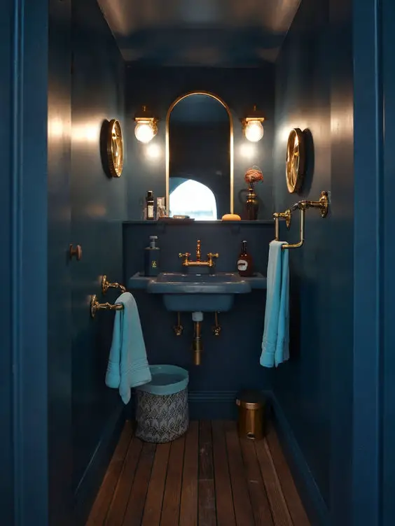 Narrow navy powder room with brass fixtures wooden flooring and wall mounted sink