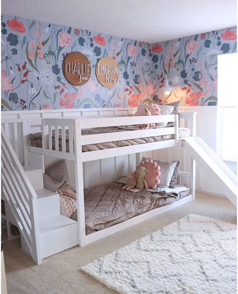 White bunk bed with stairs against floral wallpaper featuring wooden name signs