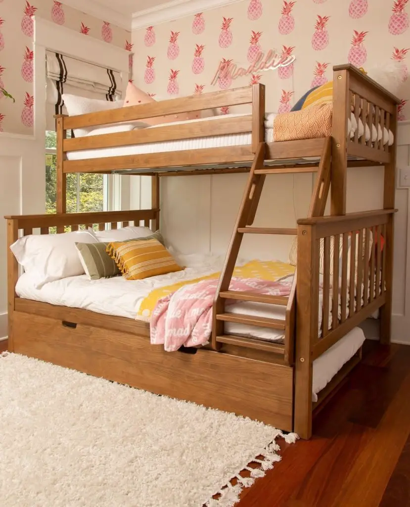 Wooden bunk bed with storage drawer against pink pineapple wallpaper and yellow accents