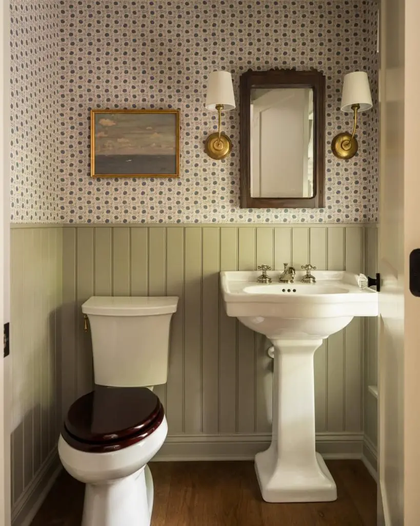 Traditional powder room featuring blue geometric wallpaper and sage wainscoting with brass fixtures