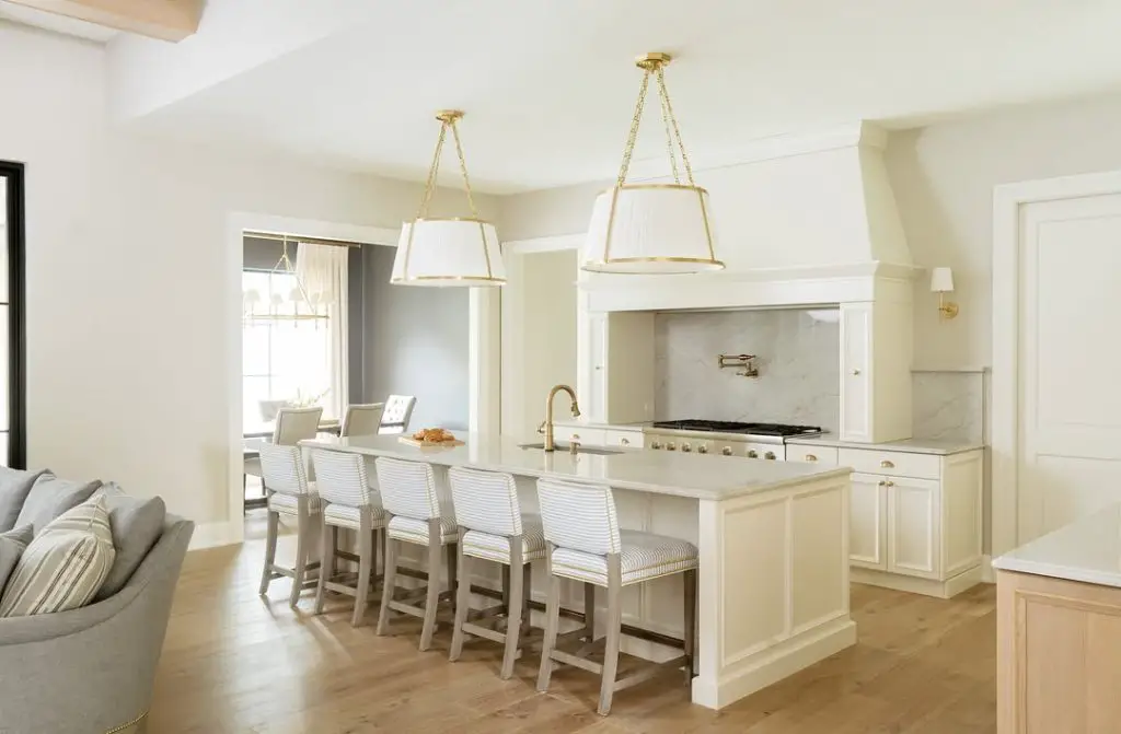 Bright white kitchen featuring striped bar stools and gold pendants