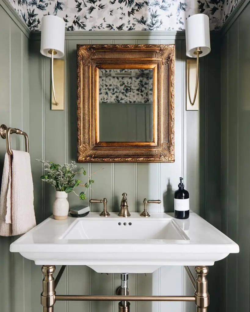Elegant powder room featuring sage green walls gold mirror and white pedestal sink