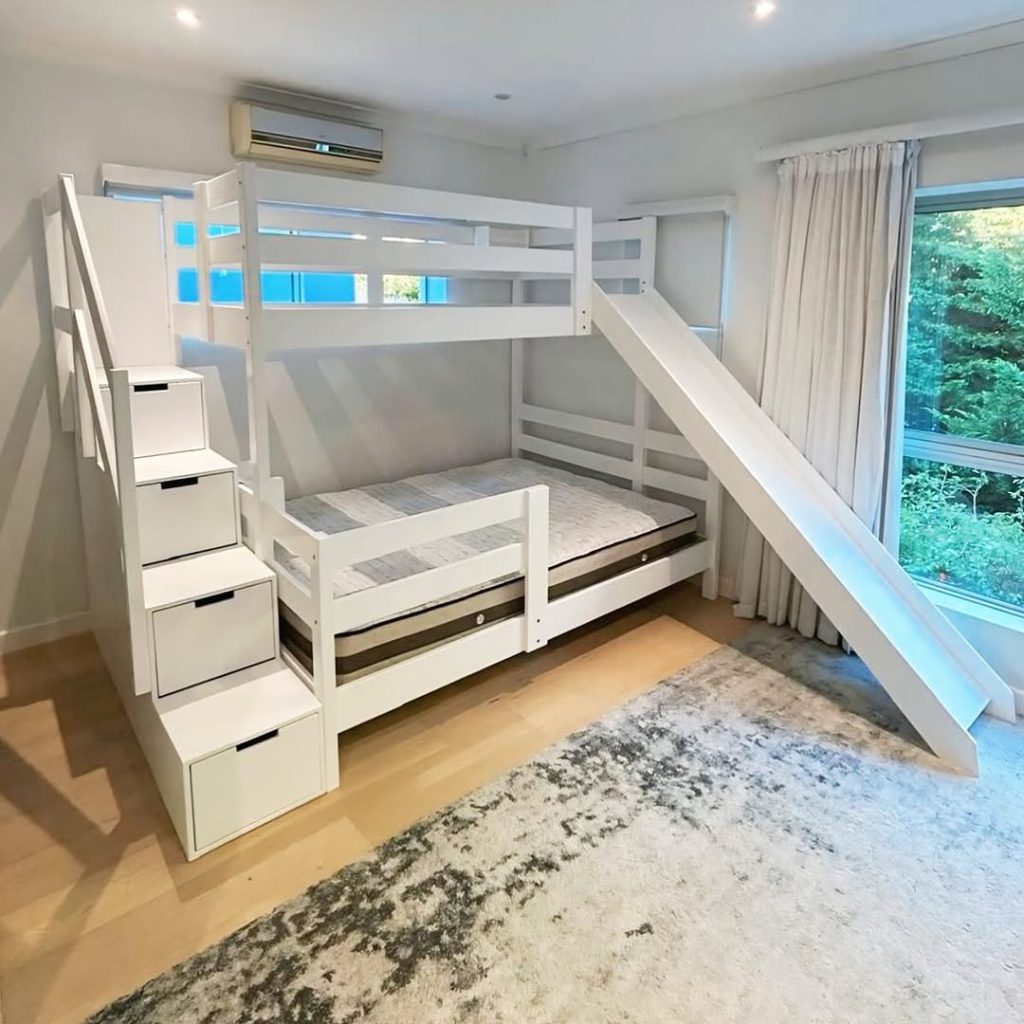 White bunk bed with storage stairs slide and trundle in bright room