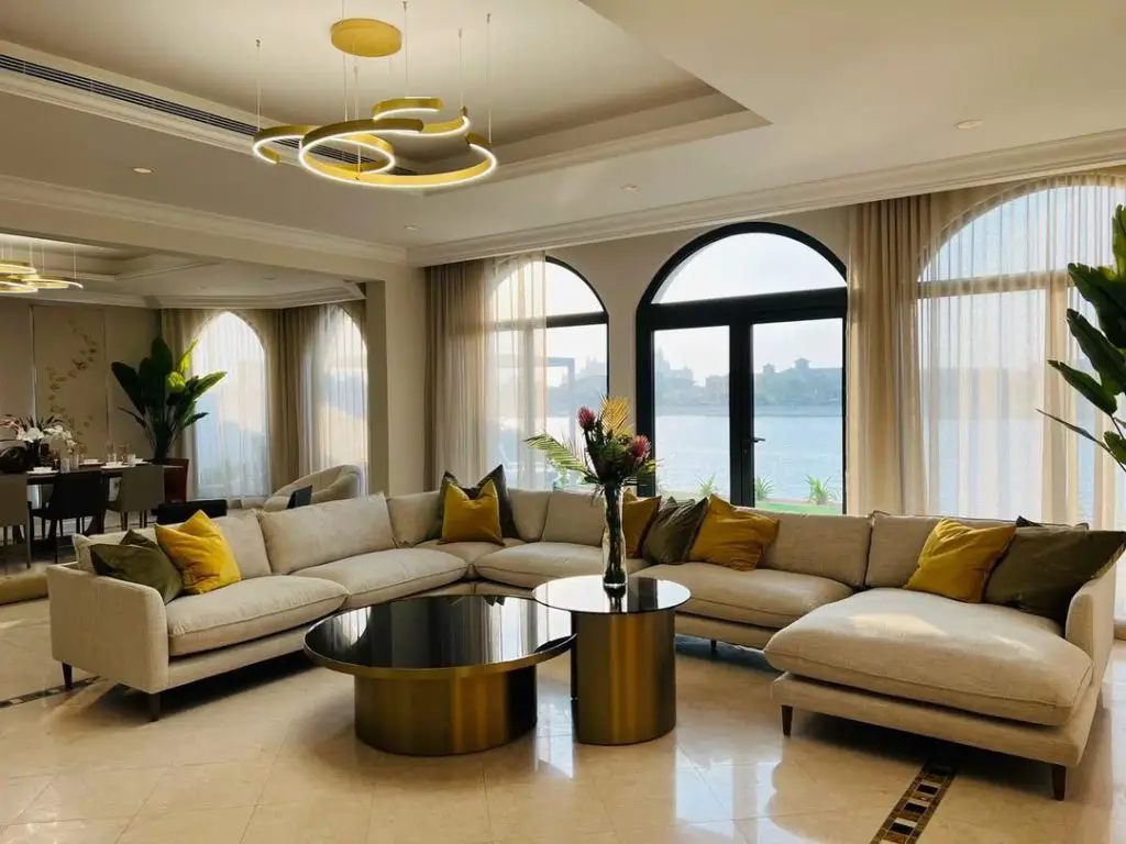 Luxurious living room with arched windows, golden chandelier, and waterfront view